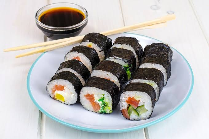 "Famous foods: Traditional Japanese sushi rolls served with soy sauce and chopsticks on a white plate.