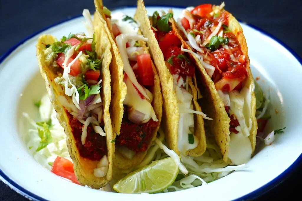 "Famous foods: Authentic Mexican tacos filled with seasoned meat, fresh vegetables, shredded cheese, salsa, and lime."