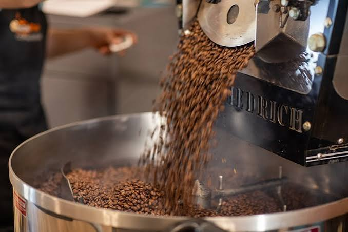 "Freshly roasted coffee beans pouring from a commercial roasting machine, showcasing the precision and craftsmanship behind premium Specialty Coffee production."